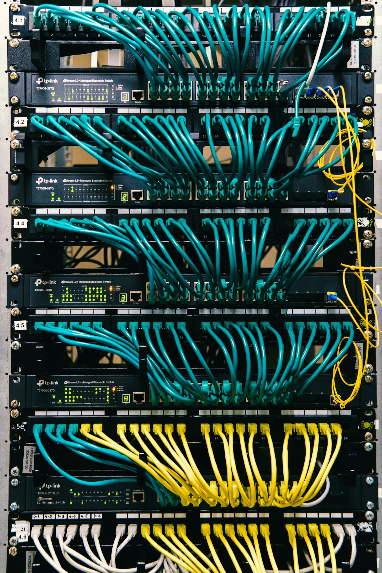 Rack de telecomunicaciones con switches administrables y cableado de red ordenado en color teal